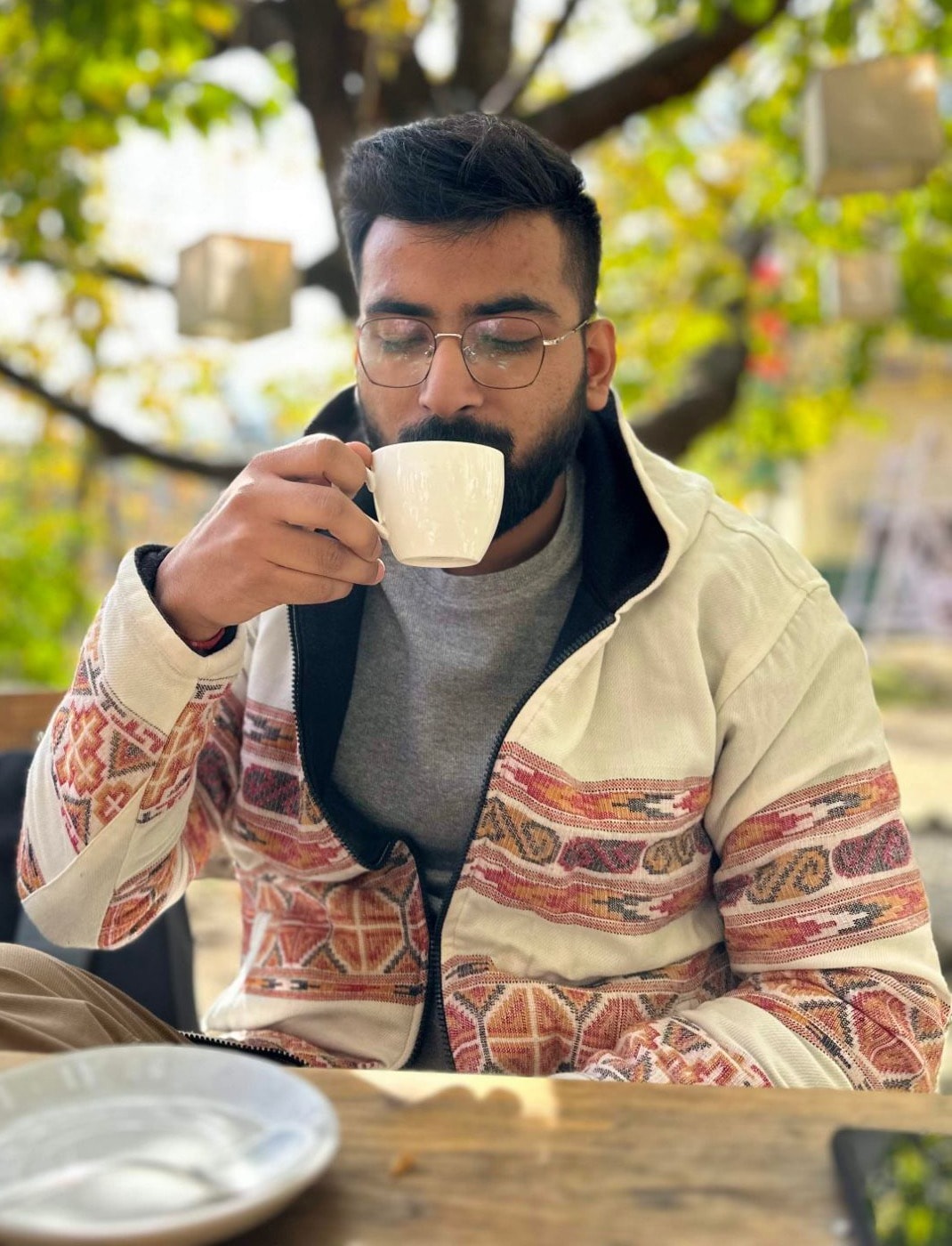 Madhur Jain drinking coffee at an outdoor table under a tree